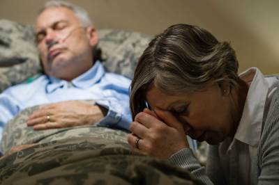Muškarac u bolničkoj postelji pored njega se žena moli 